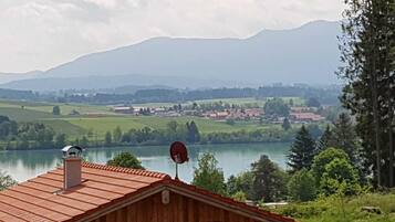 A wooden cabin with a red roof, a satellite dish, and a view of a lake and mountains in the background.