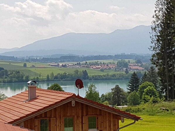 Una cabaña de madera con techo rojo, una antena parabólica y vistas a un lago y montañas al fondo.