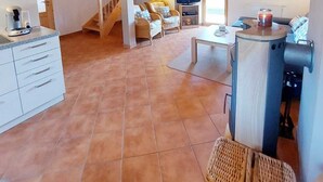 A spacious living area with a wooden ceiling, a kitchen with white cabinets, a dining table, and a fireplace. - Beautiful, cozy and comfortable vacation home on Lake Lechsee right on the edge of the forest (Lechbruck am See)