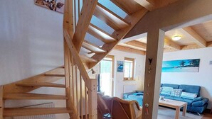 A wooden staircase leading to an upper level, a living area with a sofa and a coffee table, and a painting on the wall. - Beautiful, cozy and comfortable vacation home on Lake Lechsee right on the edge of the forest (Lechbruck am See)