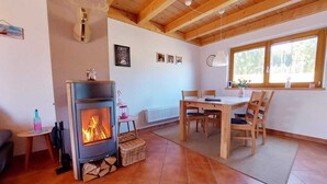 A cozy room with a wood-burning stove, a dining table with chairs, and a window with a view of trees. - Beautiful, cozy and comfortable vacation home on Lake Lechsee right on the edge of the forest (Lechbruck am See)