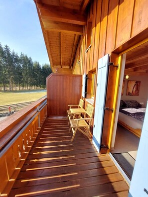 Una terraza de madera con vistas a un bosque, una cama y una puerta que da a un dormitorio.