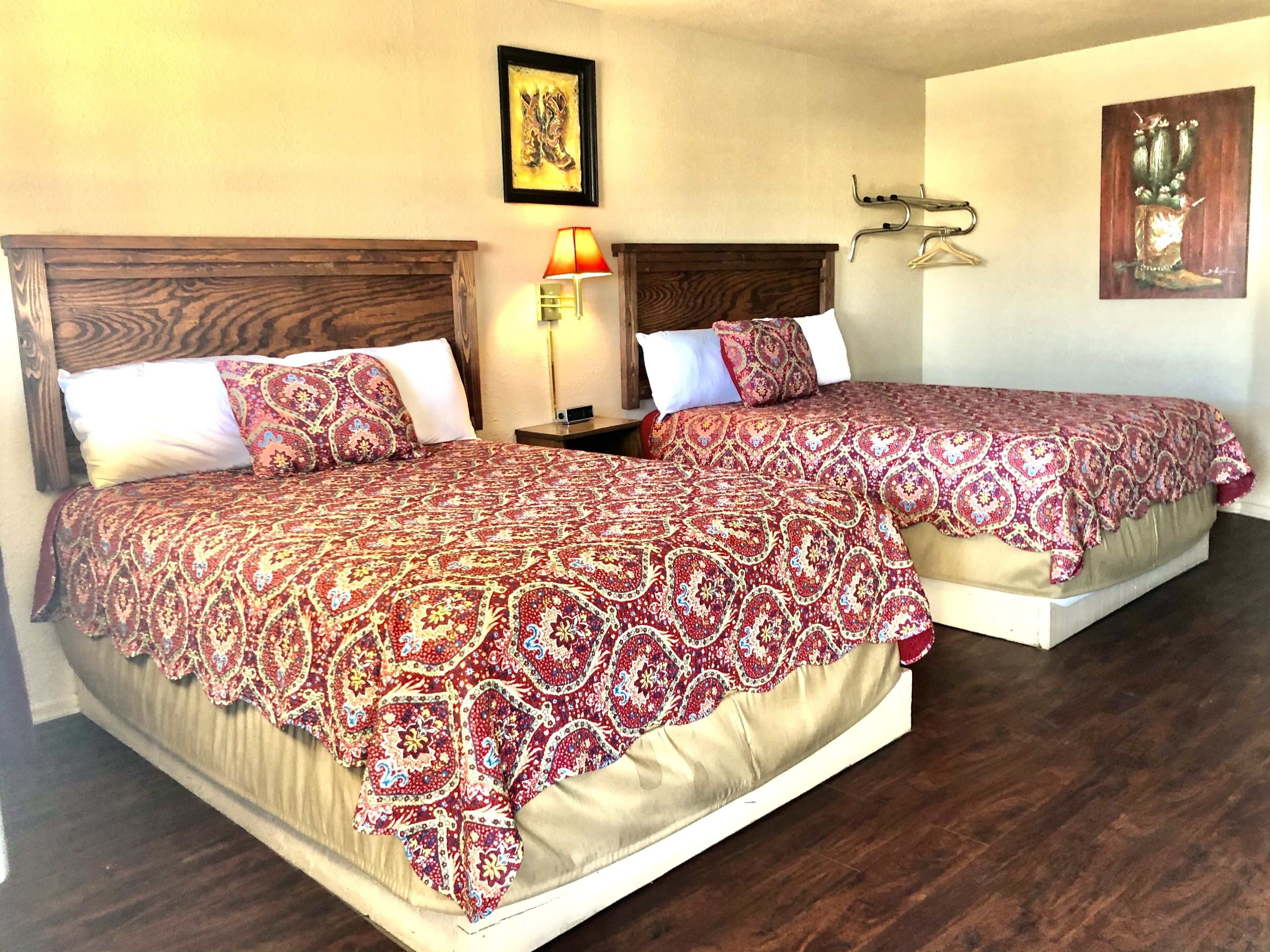 A hotel room with two beds, each with a patterned bedspread, a nightstand with a lamp, and artwork on the walls.