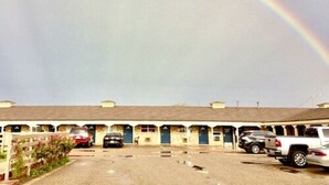 Un motel avec une rangée de chambres, un parking et un arc-en-ciel dans le ciel.
