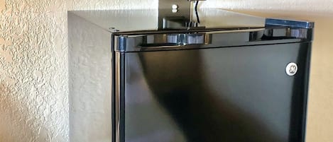 A compact, black refrigerator with a digital display on top, mounted on a textured wall.