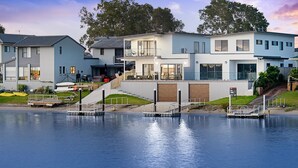 Propiedad frente al agua con casas modernas, un muelle y un cartel de 'For Sale'.