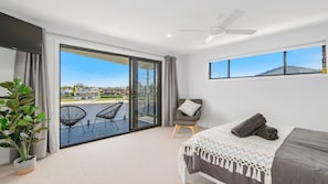 A modern bedroom with a large sliding glass door leading to a balcony, a bed with a patterned throw, a chair, and a ceiling fan. - Reflections on the water 2B River Park Road, Port Macquarie (PORT MACQUARIE)