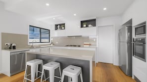 A modern kitchen with a central island, bar stools, a dishwasher, a refrigerator, and a stove.