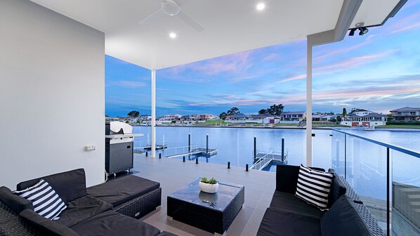 A balcony with a view of a marina, outdoor seating, and a clear sky.