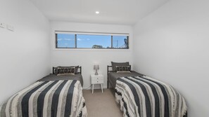 A bedroom with two single beds, a nightstand, a window, and a view of the sky.