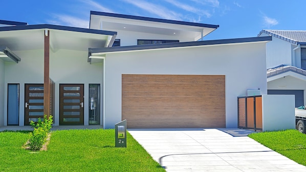 A modern two-story house with a large garage door, a driveway, and a well-maintained lawn.