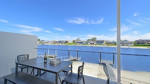 A balcony with a table and chairs overlooking a body of water with houses in the background. - Reflections on the water 2B River Park Road, Port Macquarie (PORT MACQUARIE)