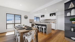 A modern kitchen with a dining area, large windows, and a view of the sea. - Reflections on the water 2B River Park Road, Port Macquarie (PORT MACQUARIE)