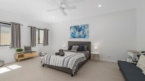 A bedroom with a bed, bedside tables, a ceiling fan, a window with curtains, and a wall-mounted painting.