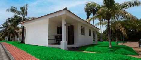 A single-story white building with a tiled roof, surrounded by green grass and palm trees.