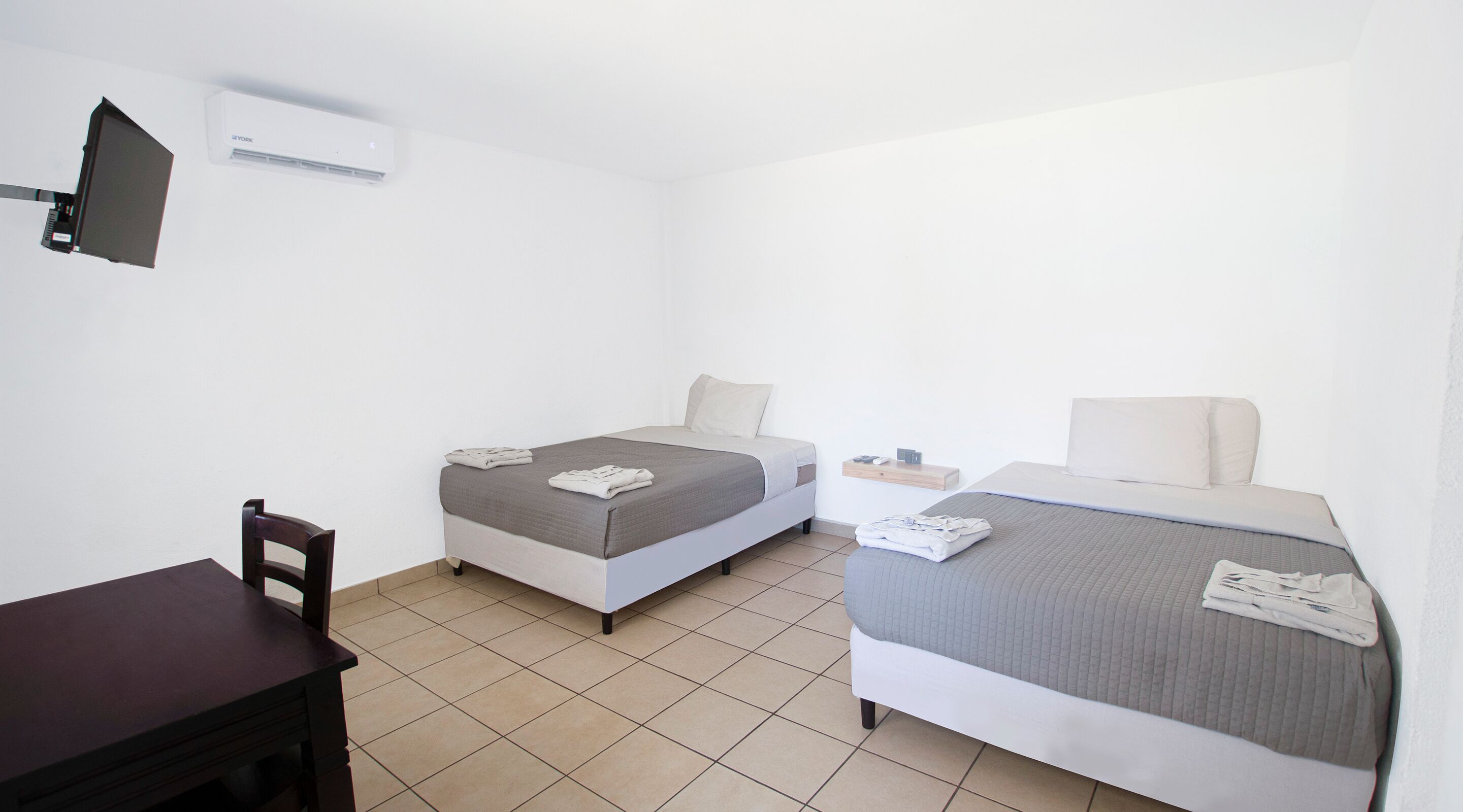 Une petite chambre propre, avec deux lits simples, un bureau et une chaise.