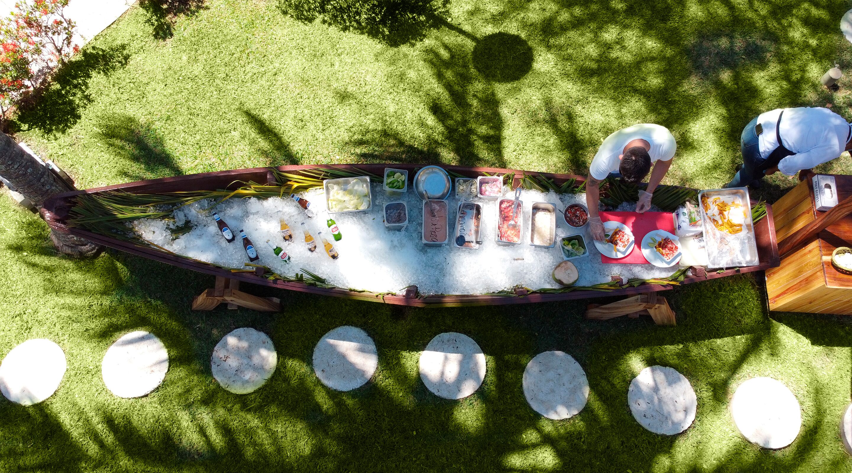 A boat-shaped ice chest filled with various food items and drinks, surrounded by a grassy area with circular stepping stones.