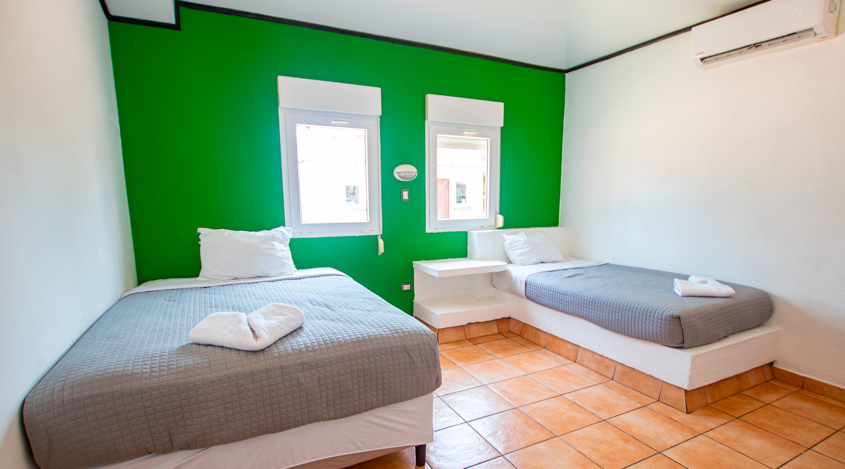 A room with two beds, green walls, white bedding, and a tiled floor.