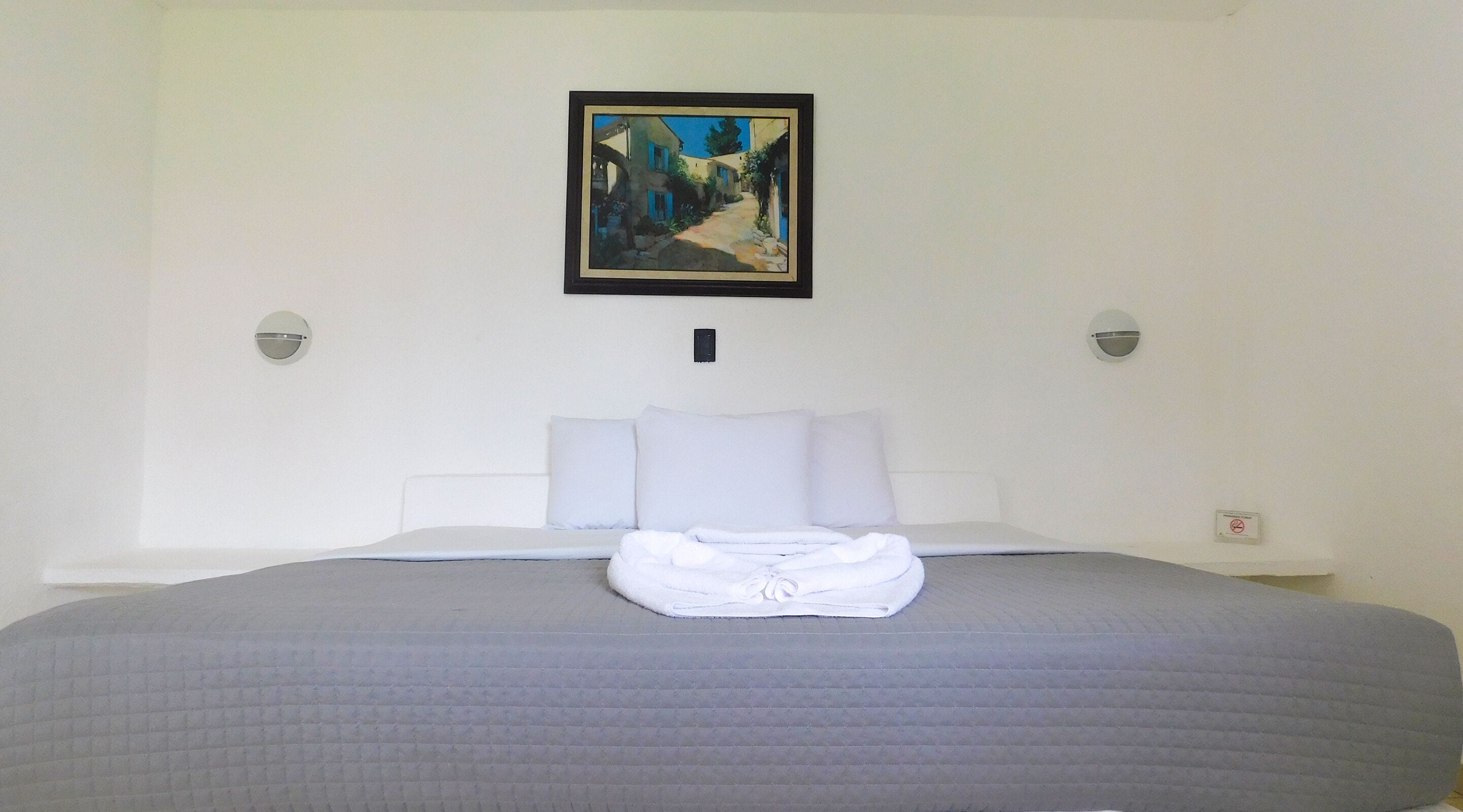 Ein Hotelzimmer mit einem Bett, einem ordentlich gefalteten weißen Handtuch und einem Gemälde über dem Bett.