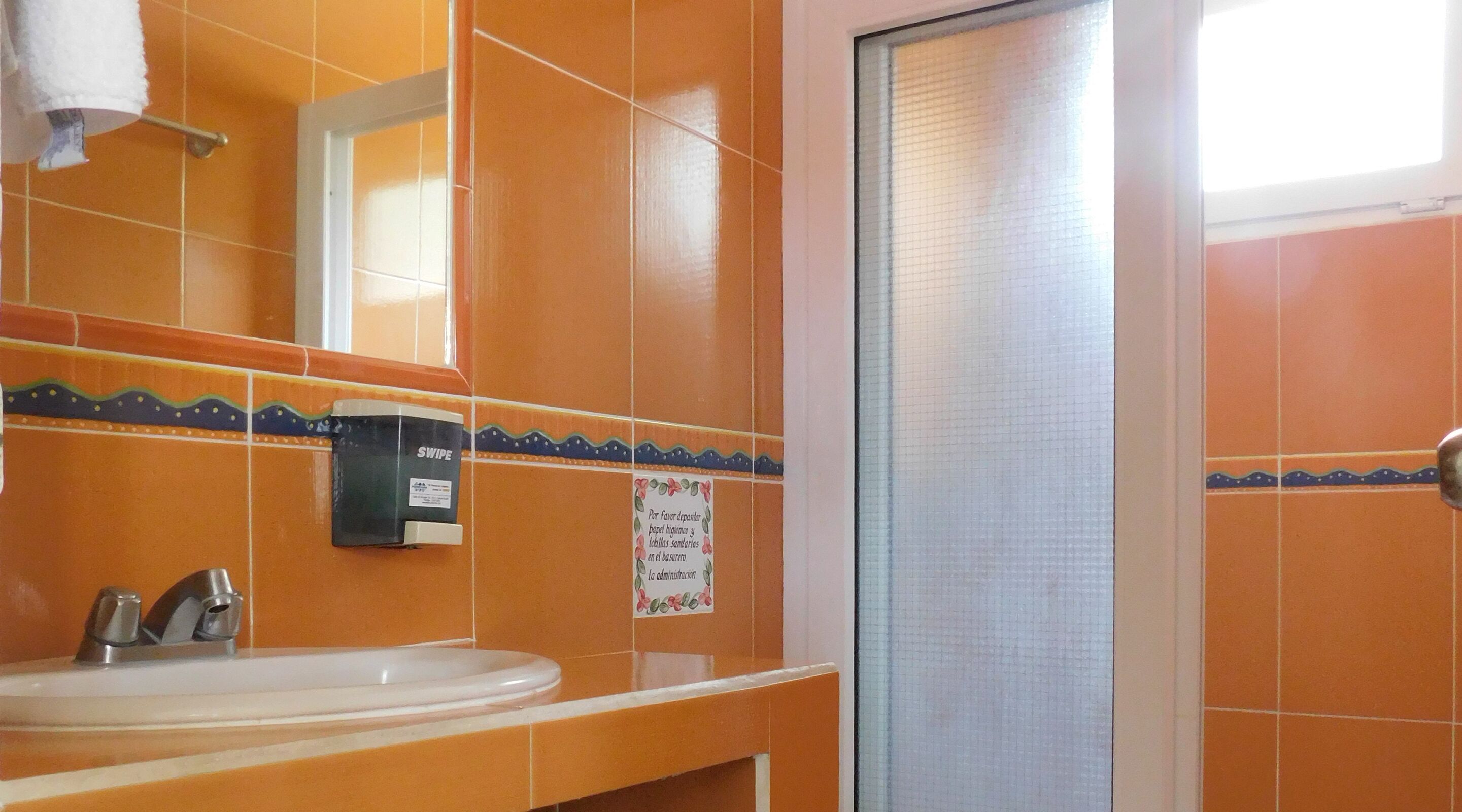 Un baño con azulejos naranjas, un lavabo blanco, un espejo y una zona de ducha.