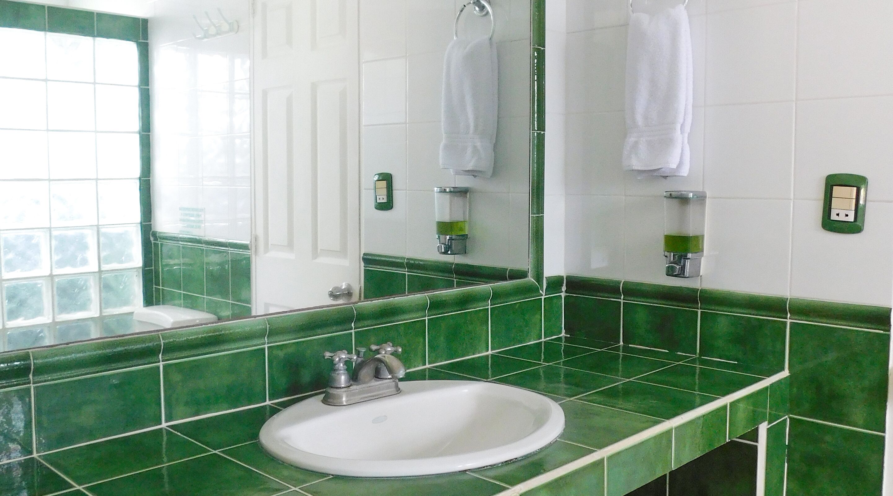 A bathroom with green tiles, a white sink, and a mirror.