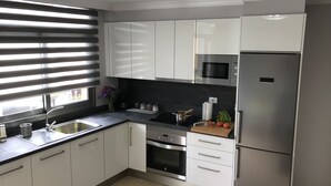Une cuisine moderne avec des meubles blancs, des appareils en acier inoxydable, un plan de travail noir et une fenêtre équipée de stores.