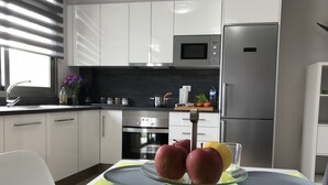 Une cuisine moderne avec des meubles blancs, un réfrigérateur en acier inoxydable, un four à micro-ondes et une table à manger agrémentée d’un présentoir de fruits.