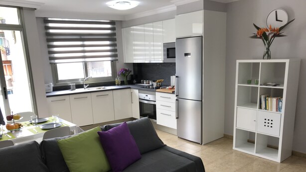Une cuisine moderne avec des meubles blancs, un réfrigérateur en acier inoxydable et un coin repas avec une table dressée pour deux personnes.