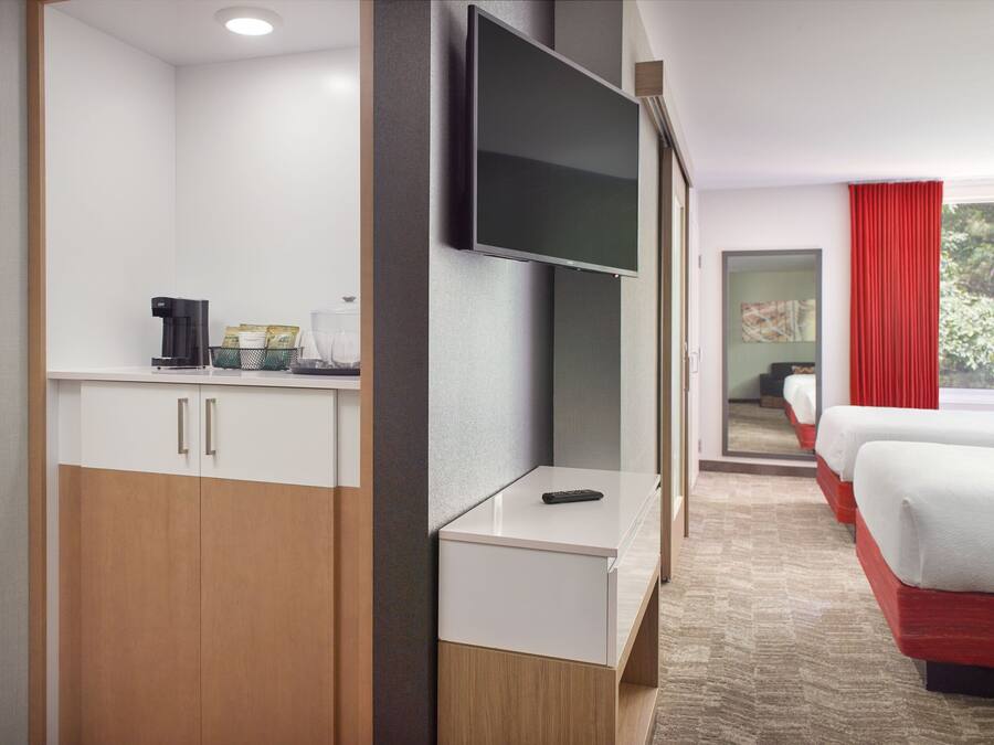 Quarto de hotel com cama, televisão, máquina de café e secretária.