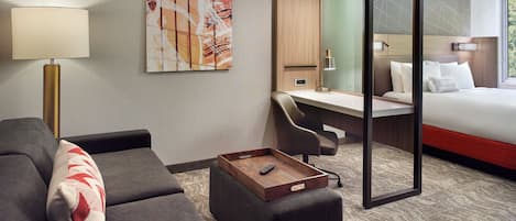A hotel room with a sofa, a desk, a bed, and a large window.