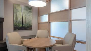 Una sala de reuniones moderna con una mesa redonda de madera, dos sillas color beige, un cuadro grande con temática de bosque en la pared y un ventanal con paneles de vidrio esmerilado.