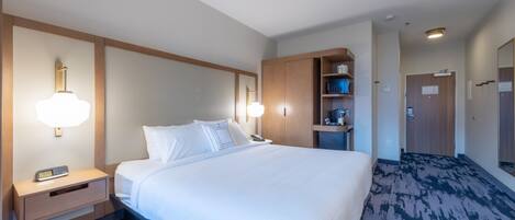 Hotelkamer met een groot bed, nachtkastjes, een lamp, een plank met toiletartikelen en een deur naar een andere kamer.