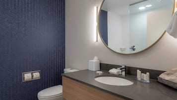Um banheiro com design moderno, com espelho redondo, toucador de madeira, pia e vaso sanitário.