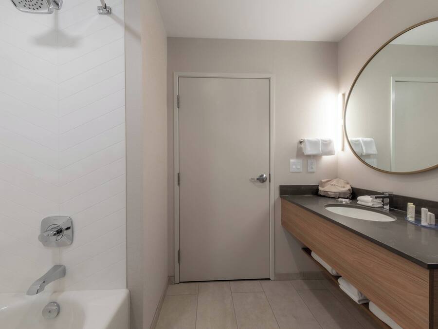 Un baño moderno con bañera, ducha, lavamanos y espejo, y una puerta.