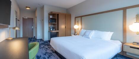 A hotel room with a large bed, a desk, a chair, a small kitchenette, and a bathroom.