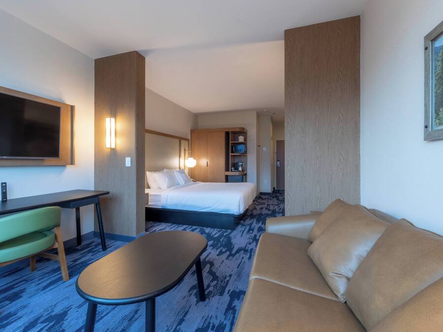 A hotel room with a bed, a desk with a chair, a sofa, and a TV.