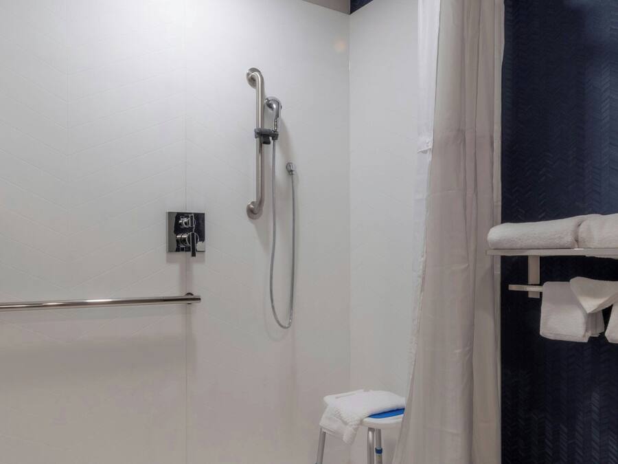 A modern bathroom with a shower, a white toilet, and a grab bar.