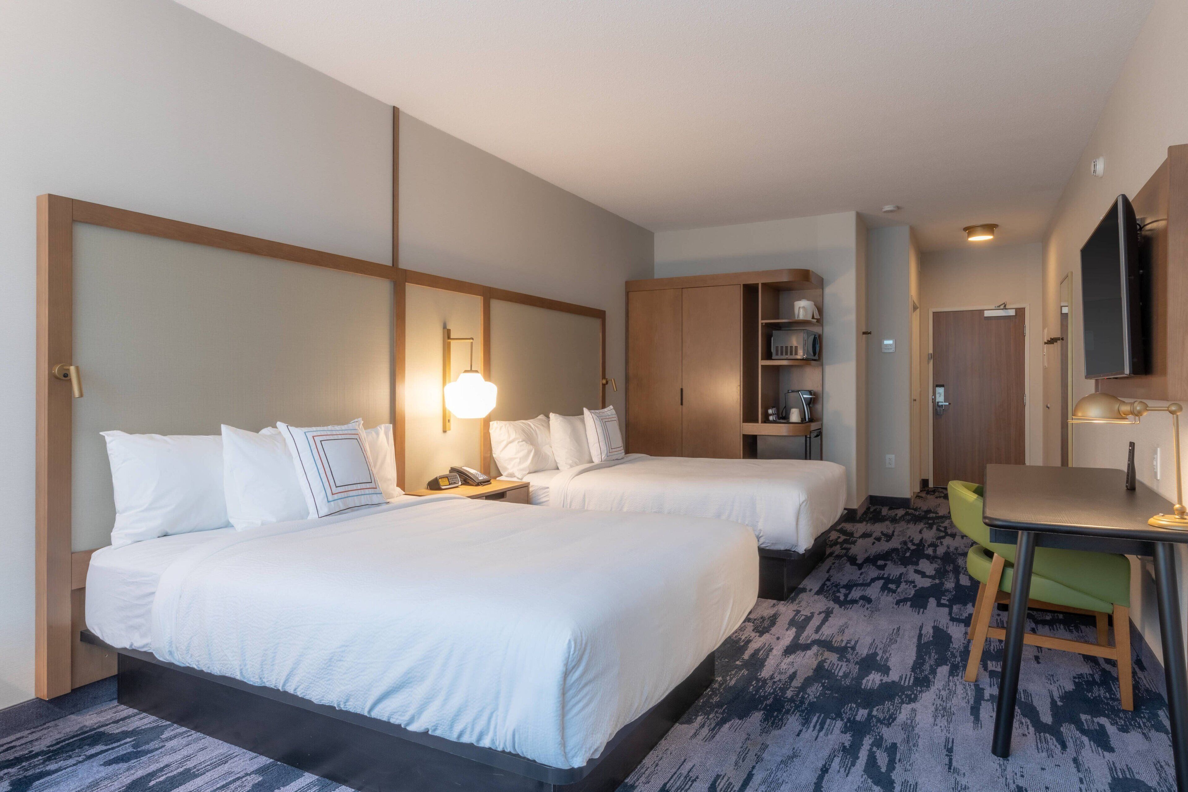 A hotel room with two beds, a desk, a chair, a TV, and a wardrobe.