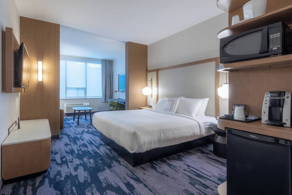 A hotel room with a bed, a desk, a microwave, and a coffee maker.