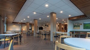 Ein geräumiges Restaurant mit mehreren Tischen und Stühlen, einem Fischgrätparkett und Pendelleuchten.