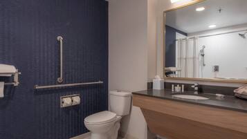Un baño moderno con una pared azul con textura, un inodoro blanco, un tocador de madera con lavabo y un espejo grande.