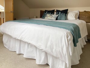 A neatly made bed with white and teal bedding, a wooden headboard, and a white wall.
