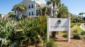 Une enseigne indiquant l’emplacement d’Atrium Villas, avec en arrière-plan un immeuble à plusieurs étages et des palmiers.