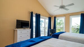 Une chambre avec deux lits, un téléviseur posé sur une commode et un balcon avec des rideaux.