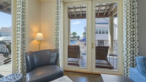 A room with a leather chair, a small table, and a lamp. There is a door leading to an outdoor area with chairs and a pool. - Pet Friendly in Seaside, Location, Large Wrap-Around Balcony, and Gulf View! (Santa Rosa Beach)