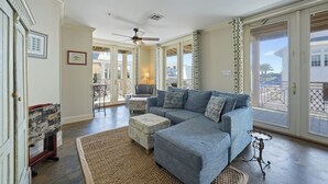 A spacious living room with a large sectional sofa, a small table, and a ceiling fan. - Pet Friendly in Seaside, Location, Large Wrap-Around Balcony, and Gulf View! (Santa Rosa Beach)