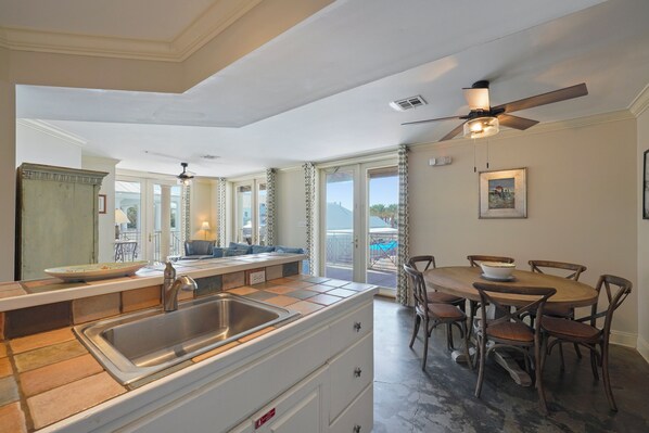 A kitchen with a large island, a dining area with wooden chairs, and a ceiling fan. - Pet Friendly in Seaside, Location, Large Wrap-Around Balcony, and Gulf View! (Santa Rosa Beach)