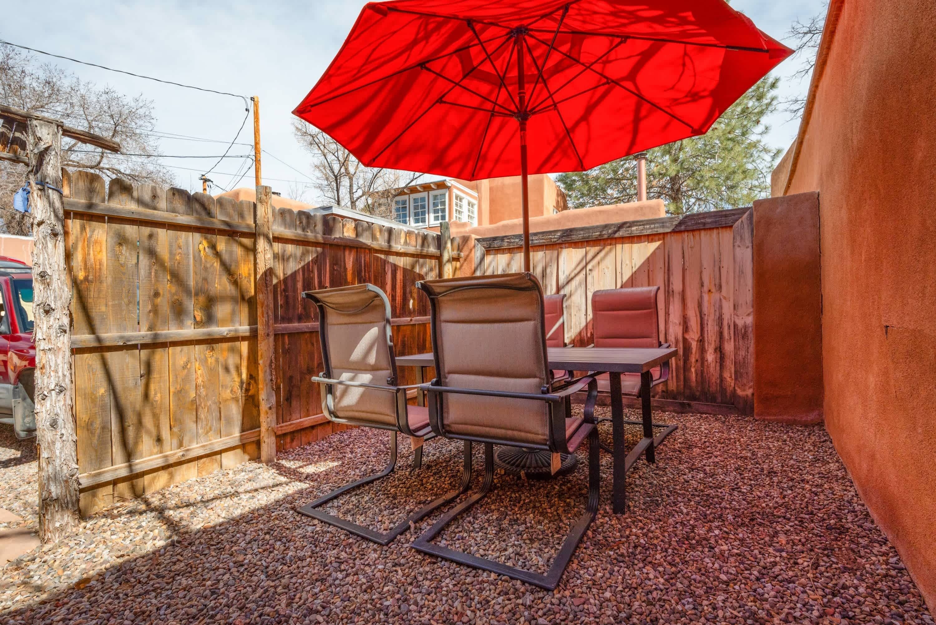 Un patio con mesa y sillas, una sombrilla roja y una cerca de madera.