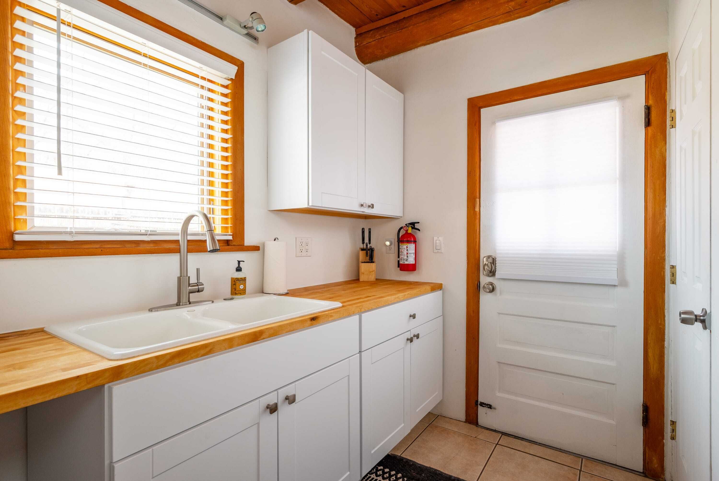 Eine Küche mit doppeltem Spülbecken, Holz Arbeitsplatte, weißen Schränken und einer Tür mit Fenster.