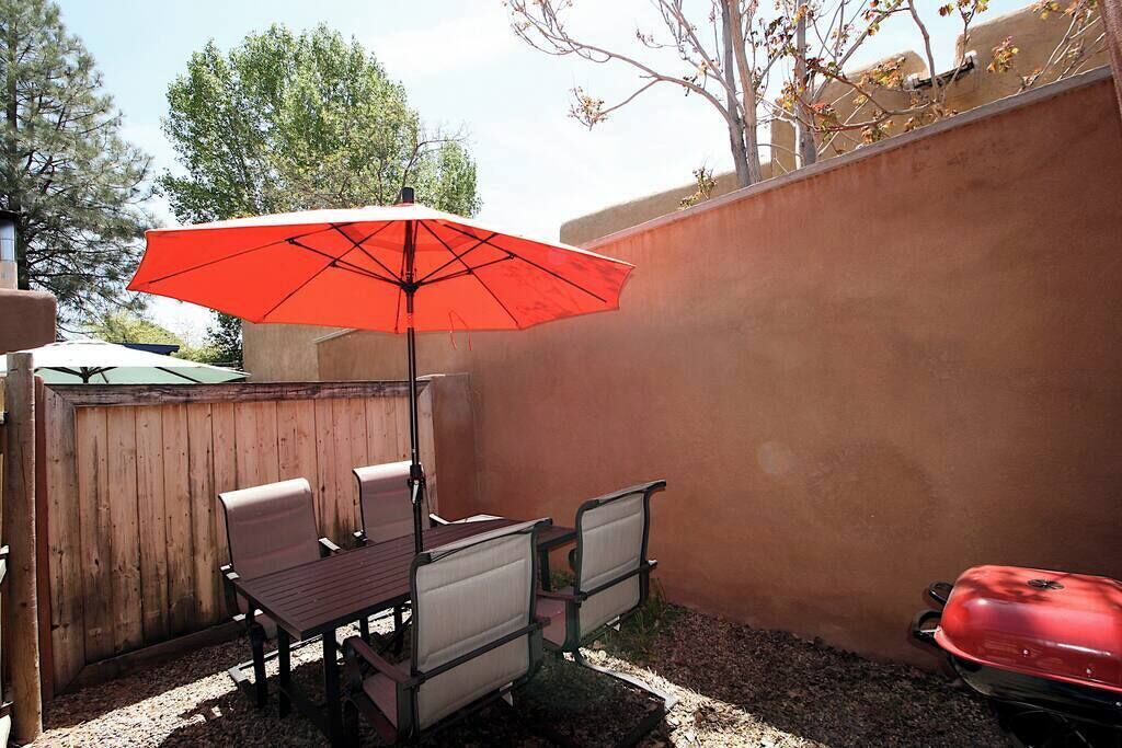 Une terrasse avec une table et des chaises, un parasol rouge et un barbecue.